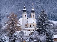 Blick vorbei an winterlichen Bäumen zur Aschauer Kirche